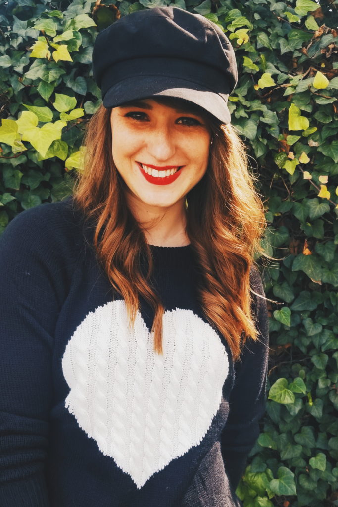 girl smiling wearing a hat and sweater with a white heart on it