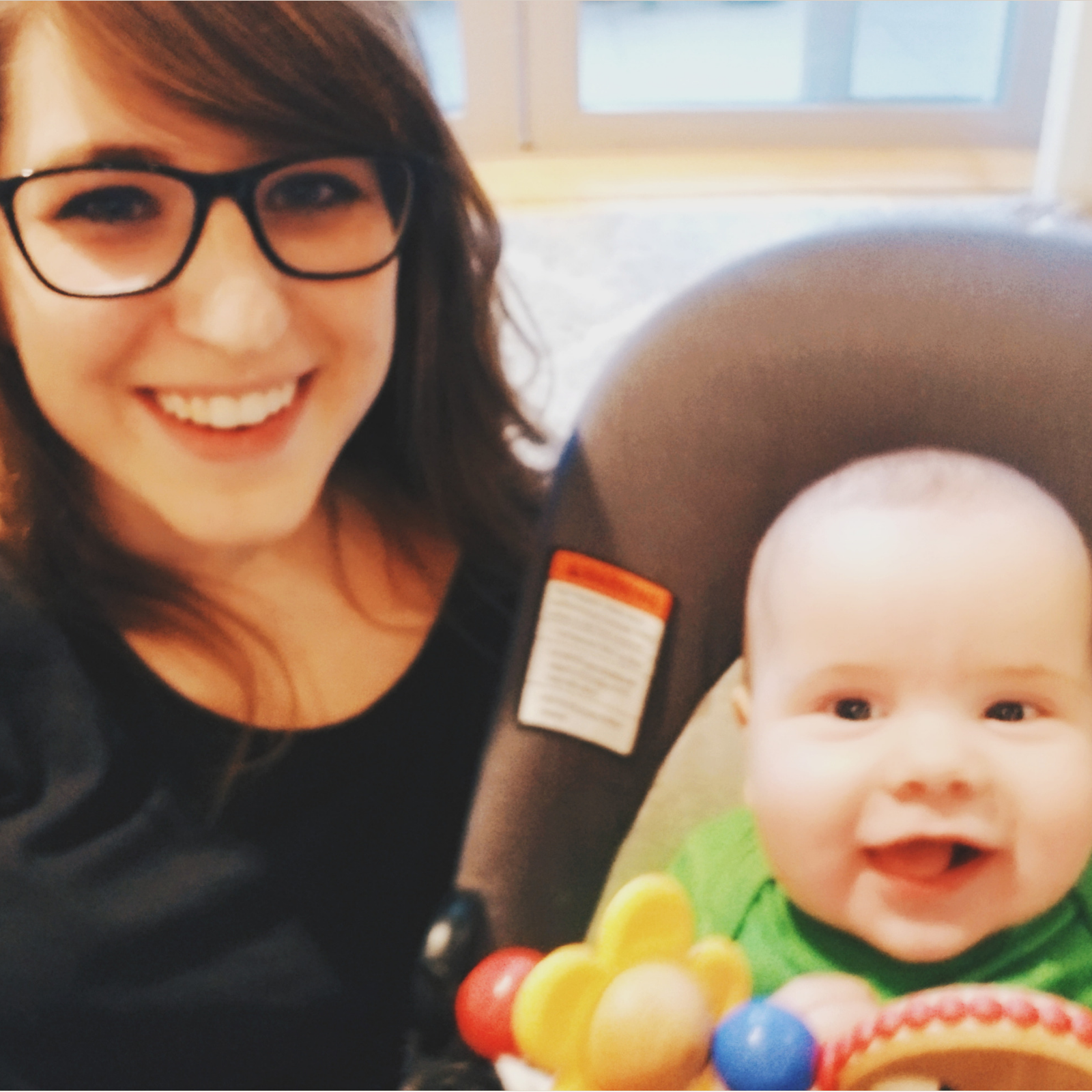 A girl wearing glasses, smiling next to a smiling baby