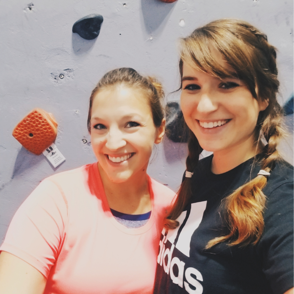 Two girls smiling, standing in front of a rock wall
