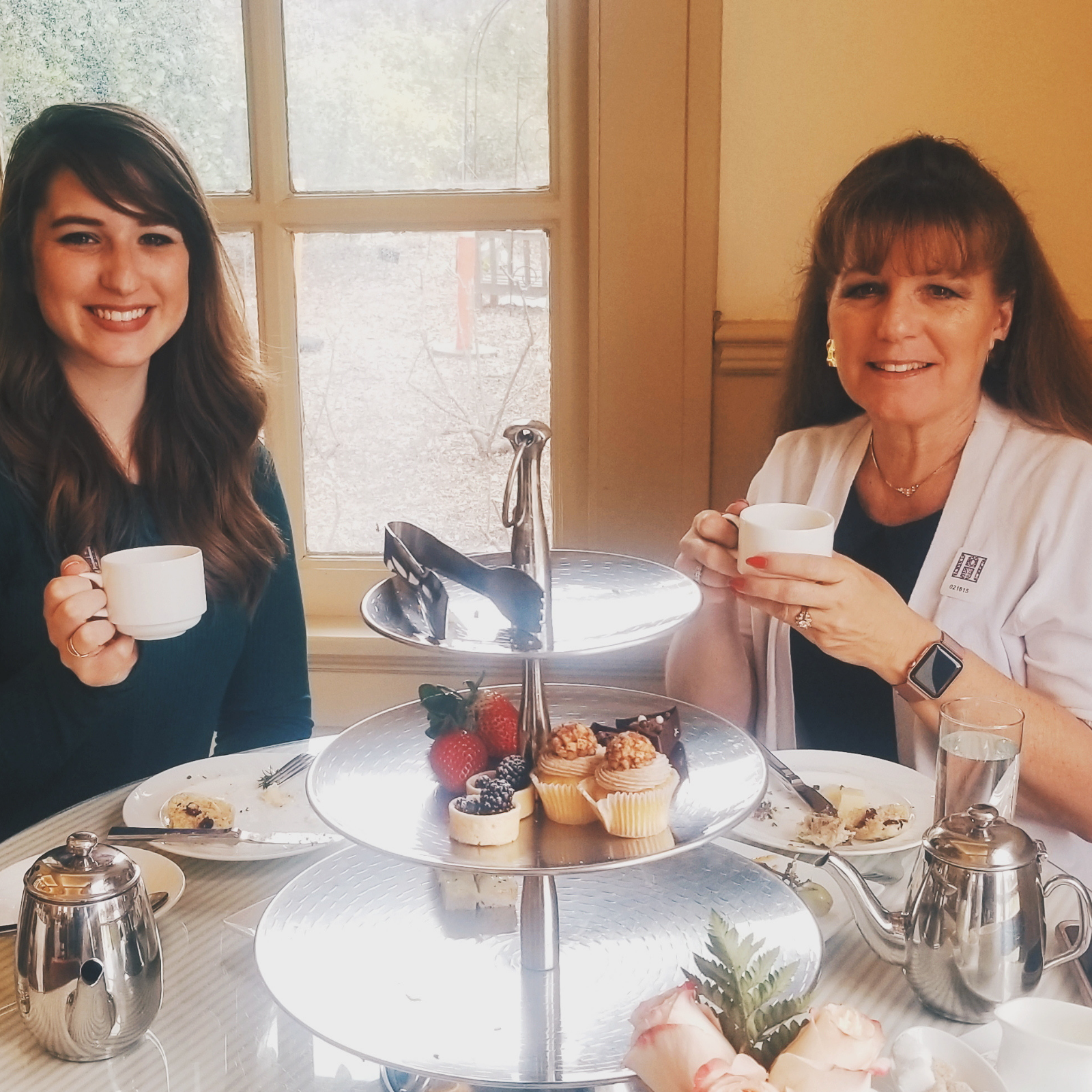 A mom and daughter smiling while sitting at a table, holding tea