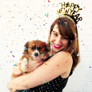 A girl holding a cute dog, wearing a Happy New Year crown with confetti falling down