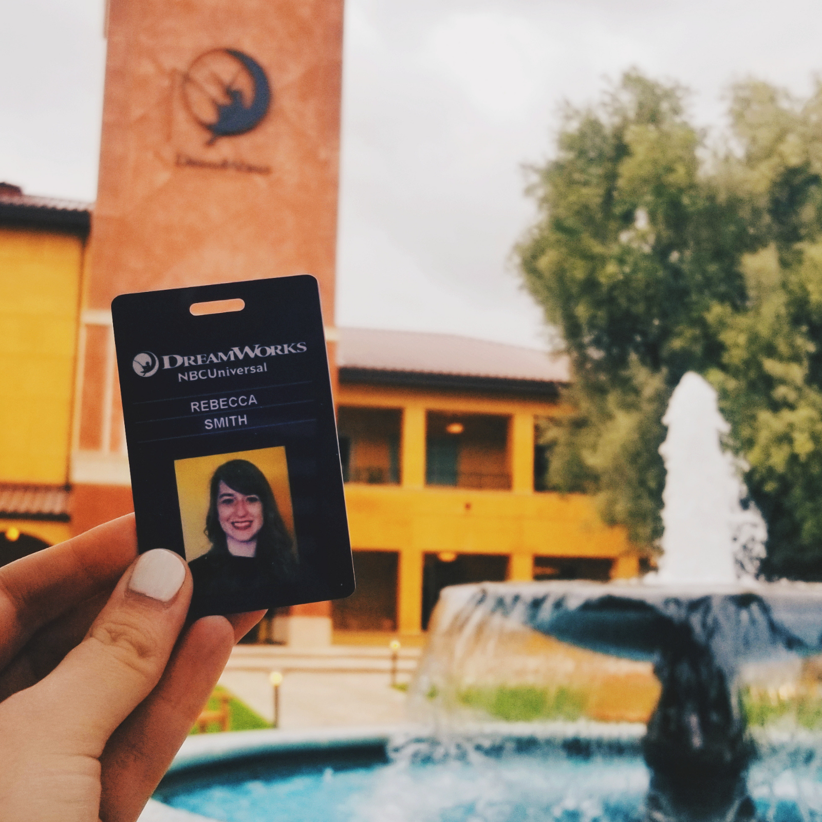 A DreamWorks employee badge in front a fountain and a building that has the DreamWorks logo on it